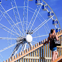 En kvinna som går uppför en trätrappa framför ett stort pariserhjul mot en blå himmel.