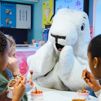 Barn som äter glass tillsammans med en stor vit sälmaskot i ett café.