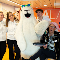 En grupp människor poserar glatt tillsammans med en stor sälmaskot i ett färgglatt lekrum.