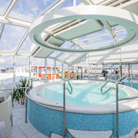 En stor bubbelpool under ett glastak på ett däck med utsikt över havet.