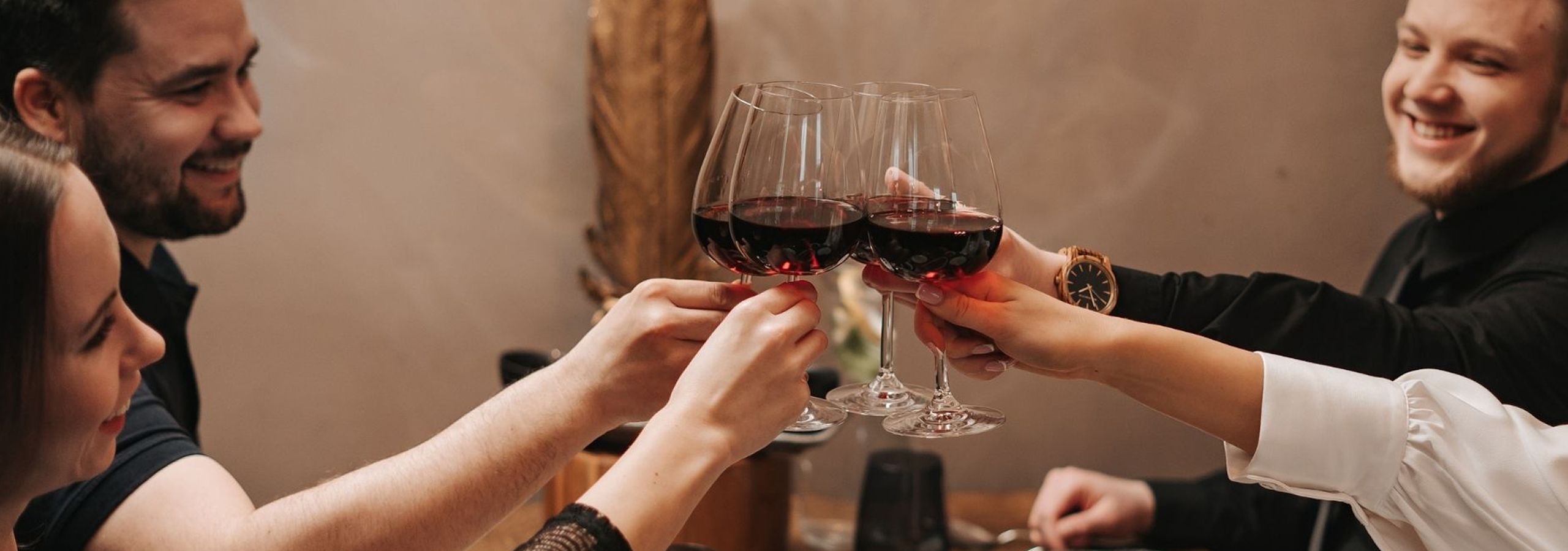 Neljä vierasta kilistää punaviinilaseja pöydässä, hymyillen.