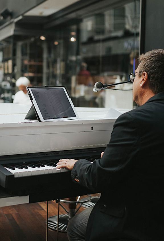 Man i svart kostym spelar på vitt piano.