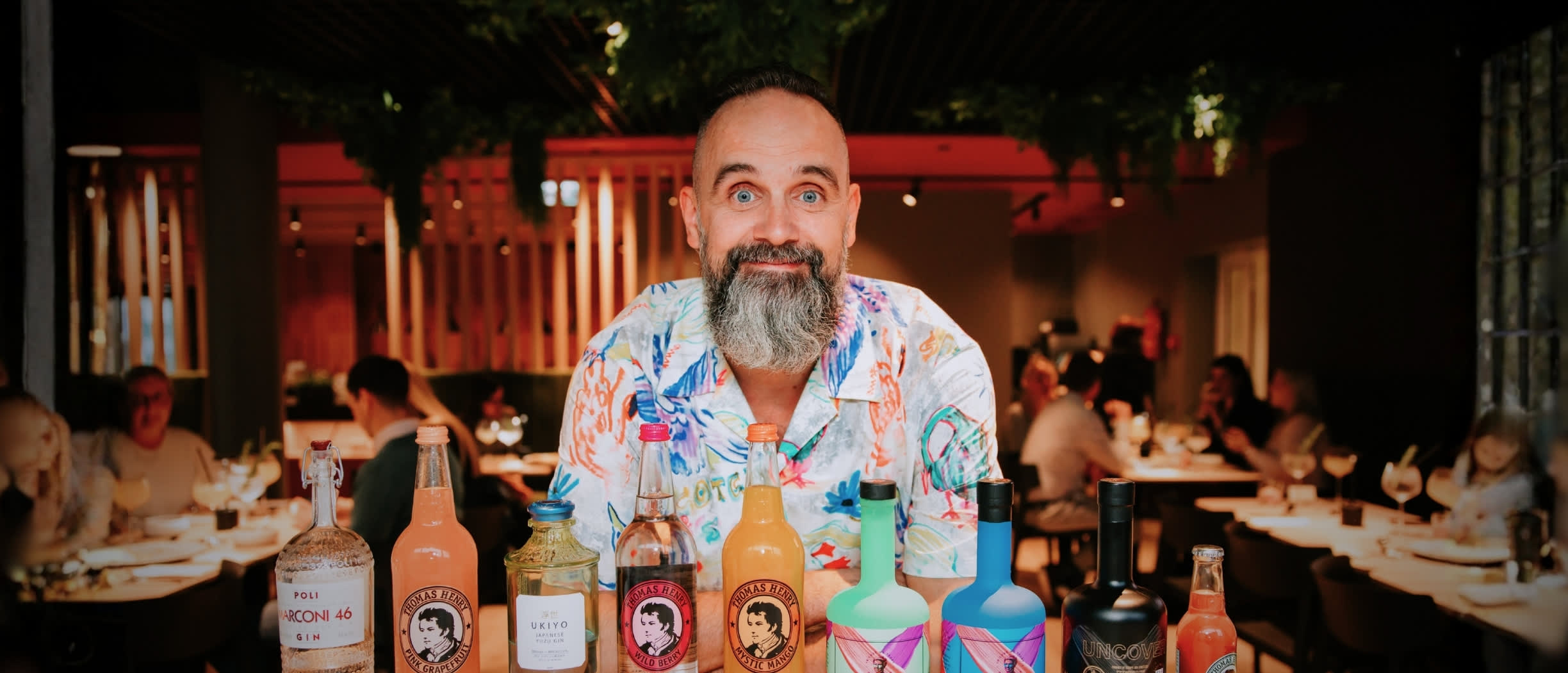 The gin instructor is posing behind gin bottles and tonic water bottles.