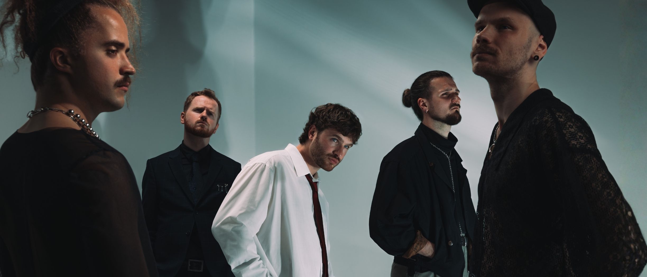 Four male performers in dark stage outfits posing against a smoky blue background, creating a modern and dramatic concert atmosphere.