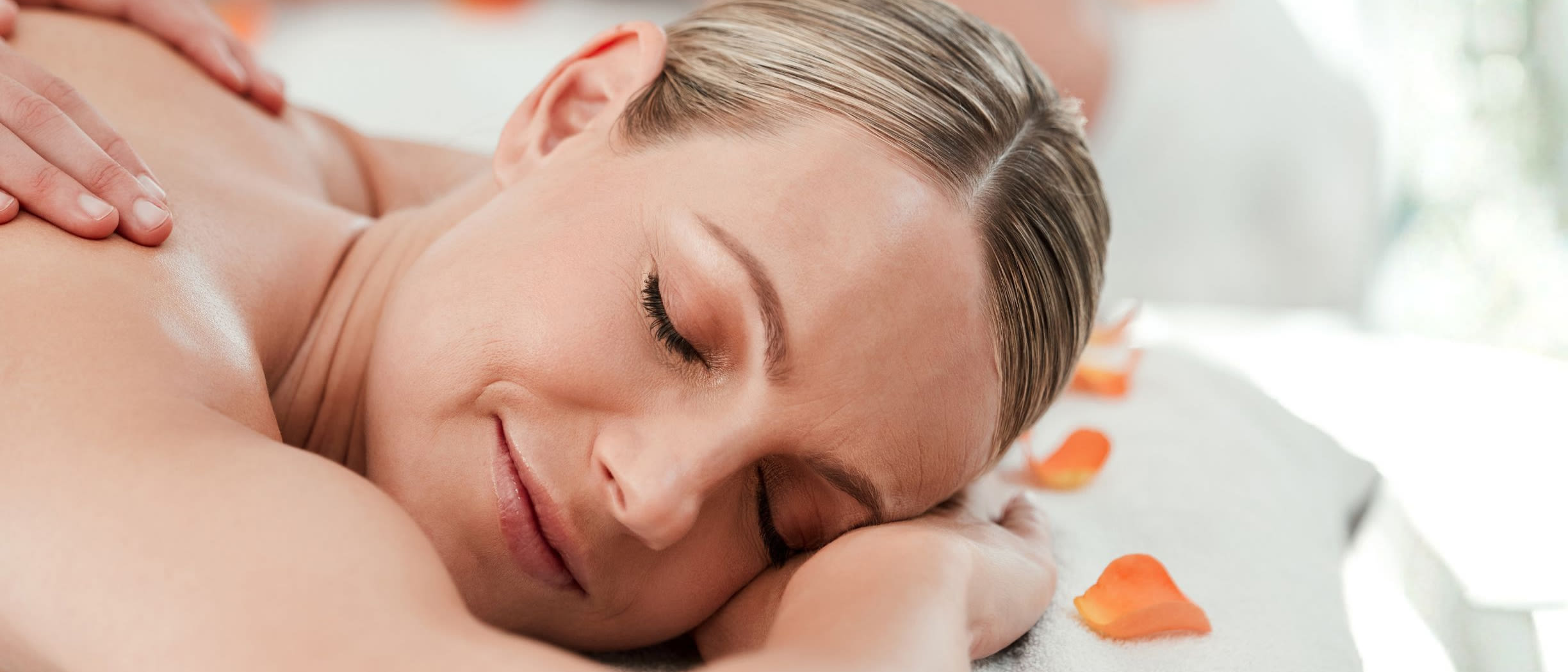 A couple enjoying a dual massage in a fair toned room, there are rose petals on the sheets.