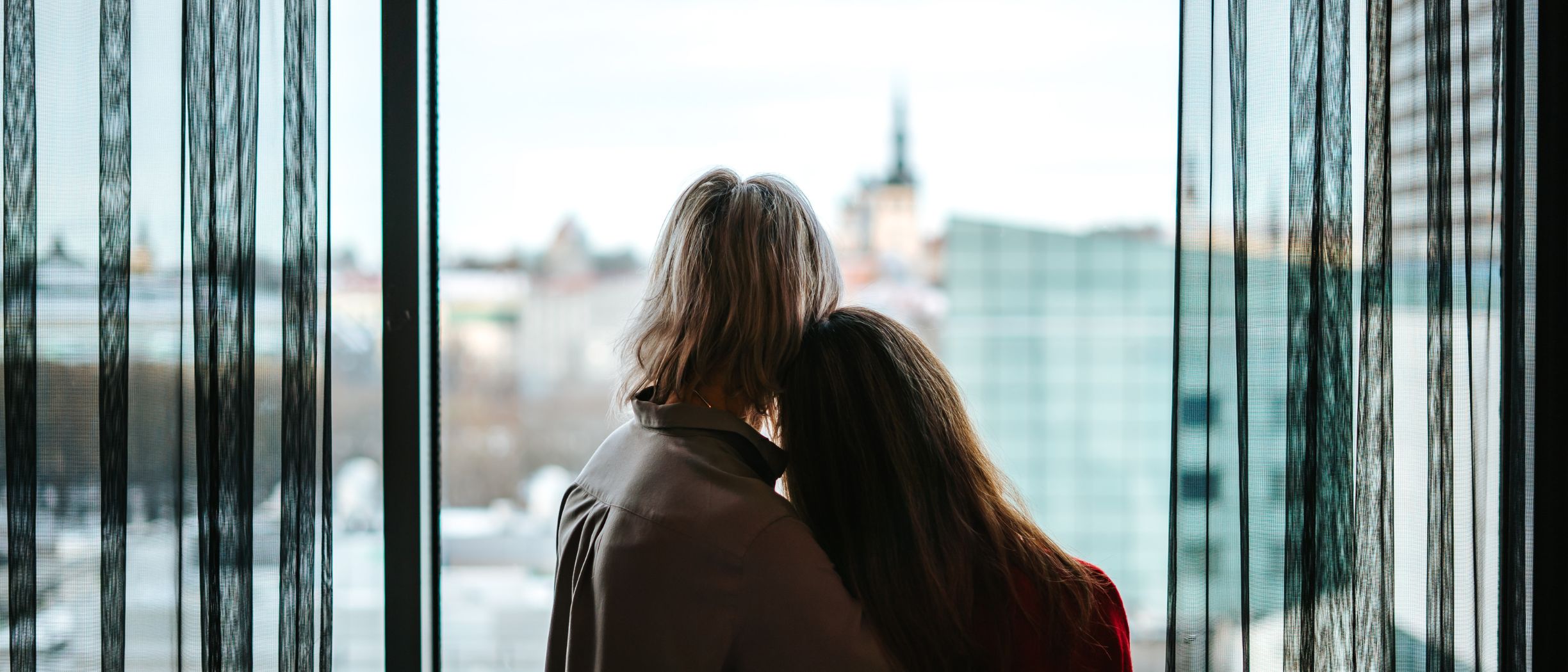 Mom and daugther looking at the city line from a window.