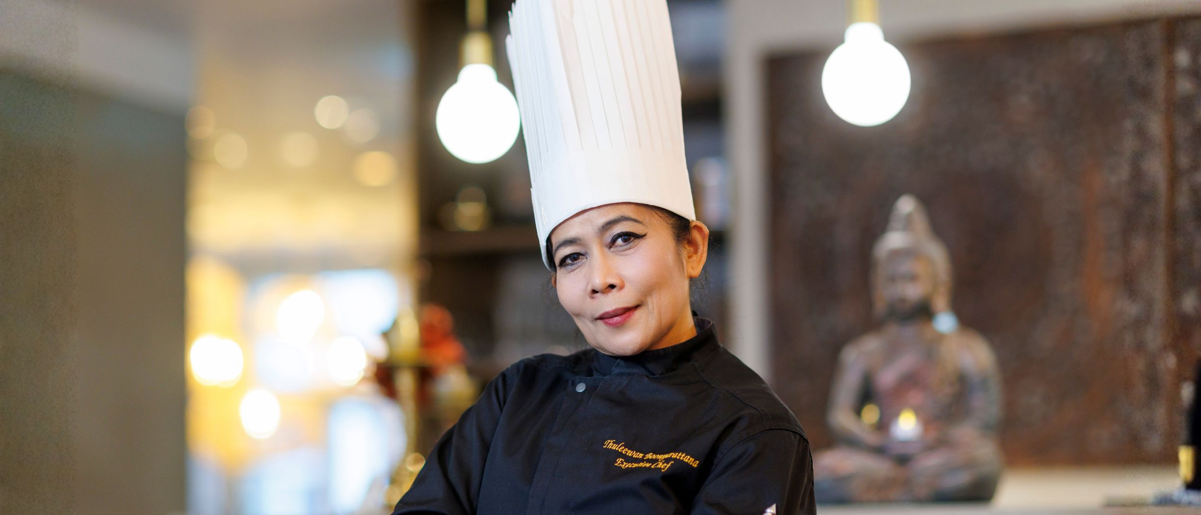 NOK NOK’s Executive Chef Thuleewan Boonyarattana in a tall white chef’s hat and a black chef’s jacket