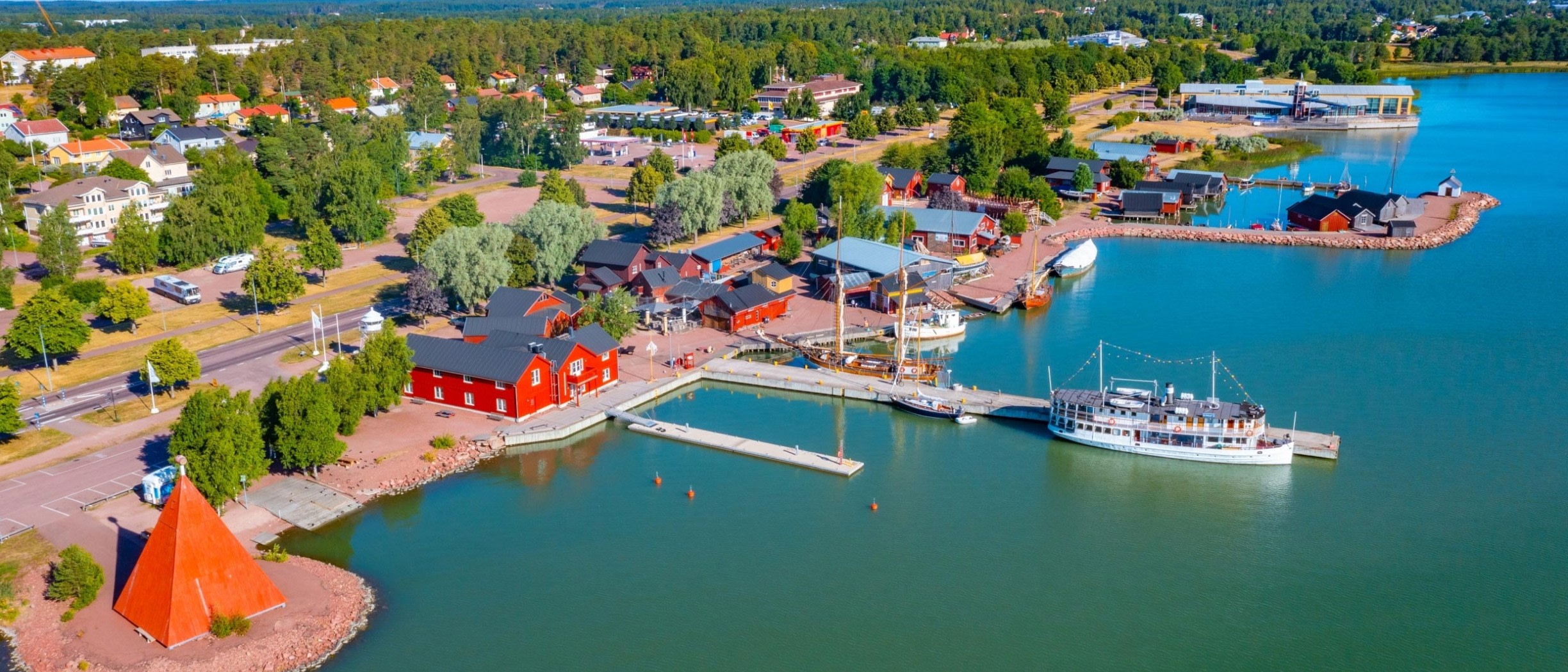 Luftaufnahme des Hafens von Mariehamn, Åland, mit Uferpromenade, roten Gebäuden und Booten am Pier