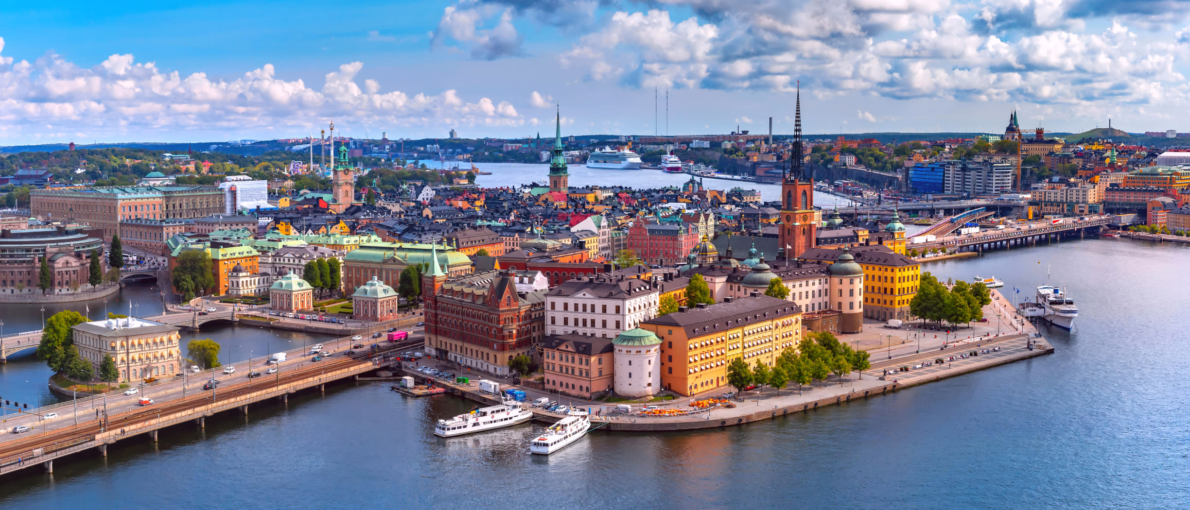 Ilmakuva Tukholman rantamaisemasta, jossa on historiallisia rakennuksia, laivoja ja auringonlasku.