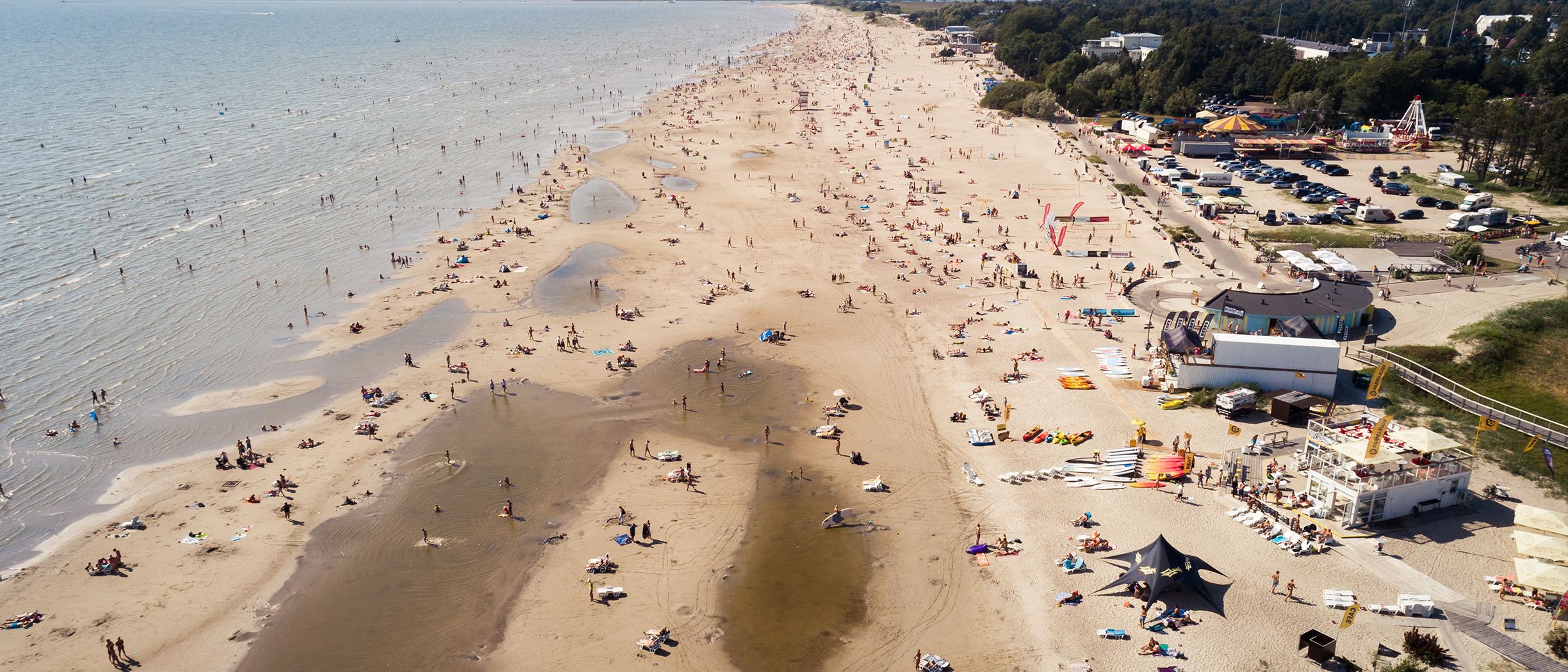 Aerial view of Pärnu Beach in summer, long sandy shoreline with swimmers, sunbathers and beach bars
