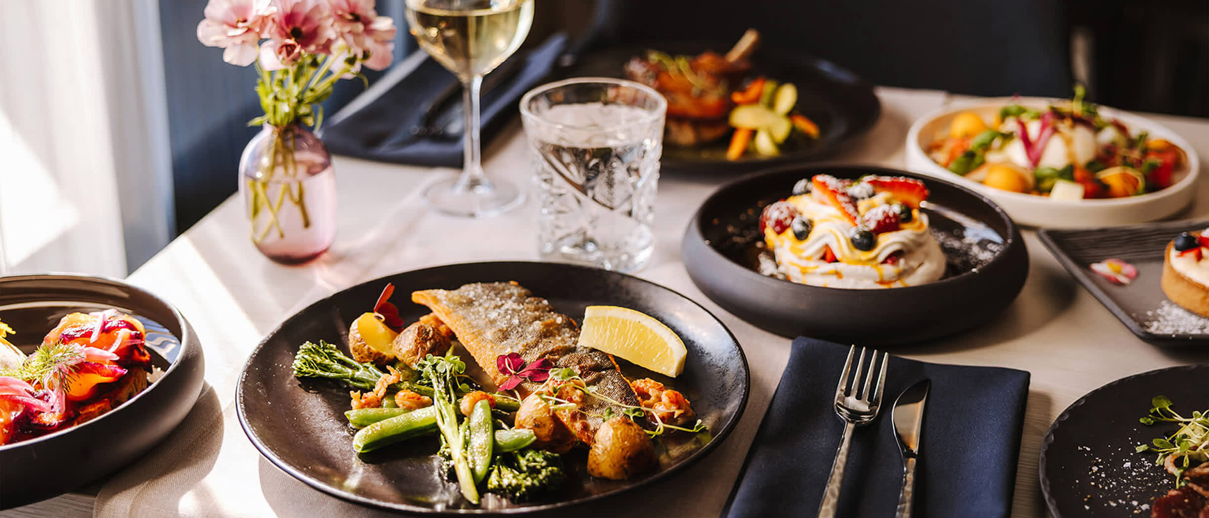 Plated fish dish, salads, desserts and white wine at The Chef’s Kitchen restaurant on MyStar.