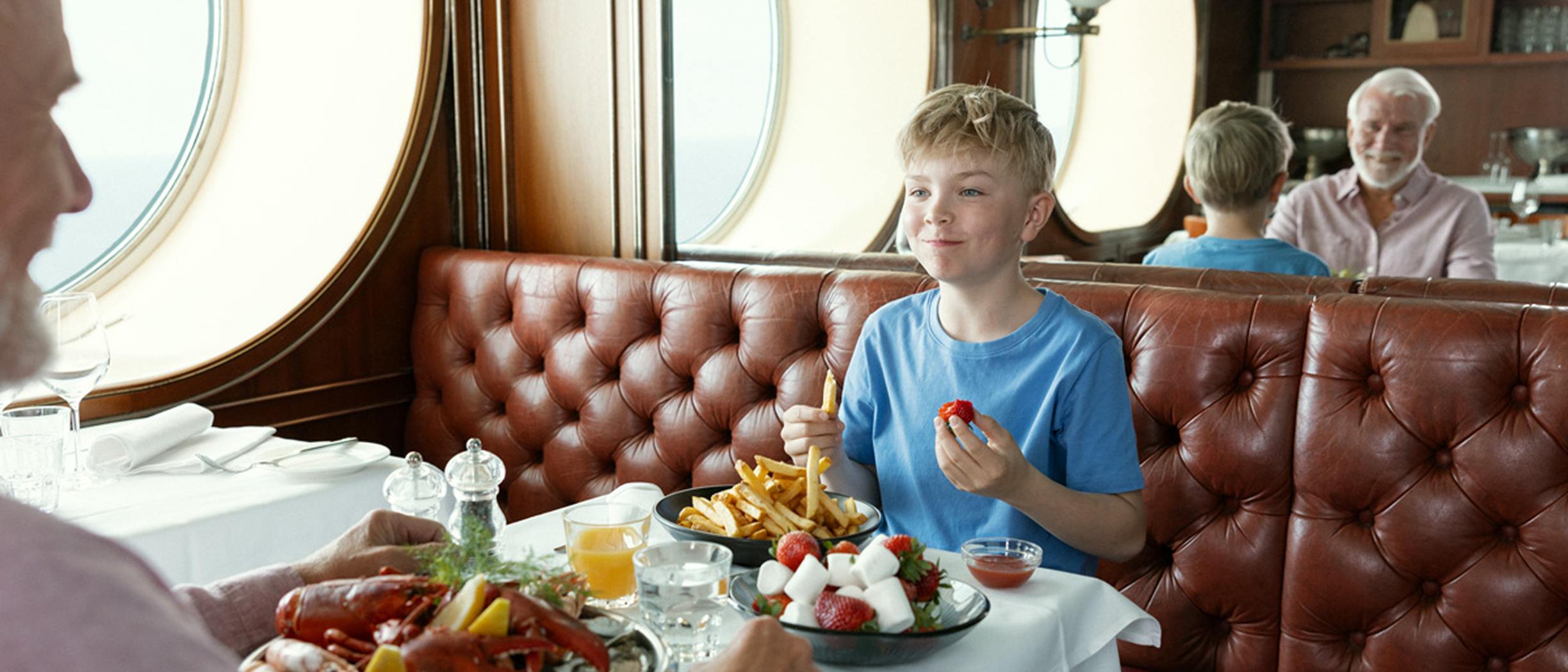 En pojke håller upp två jordgubbar framför ögonen för att busa med sin morfar i restaurang Happy Lobster på Silja Symphony