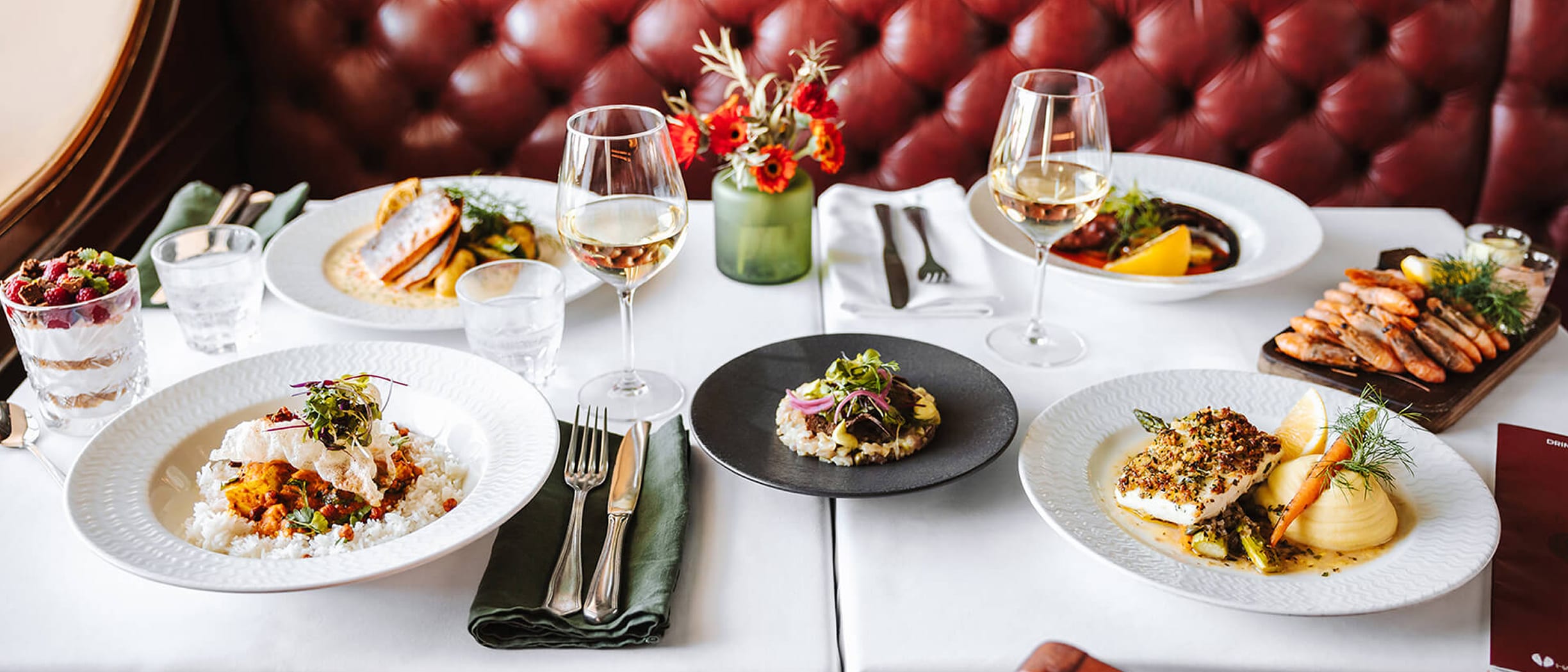 A beautifully set table at Happy Lobster restaurant on a Tallink Silja ship, featuring elegant seafood dishes, wine glasses and a warm, inviting atmosphere.