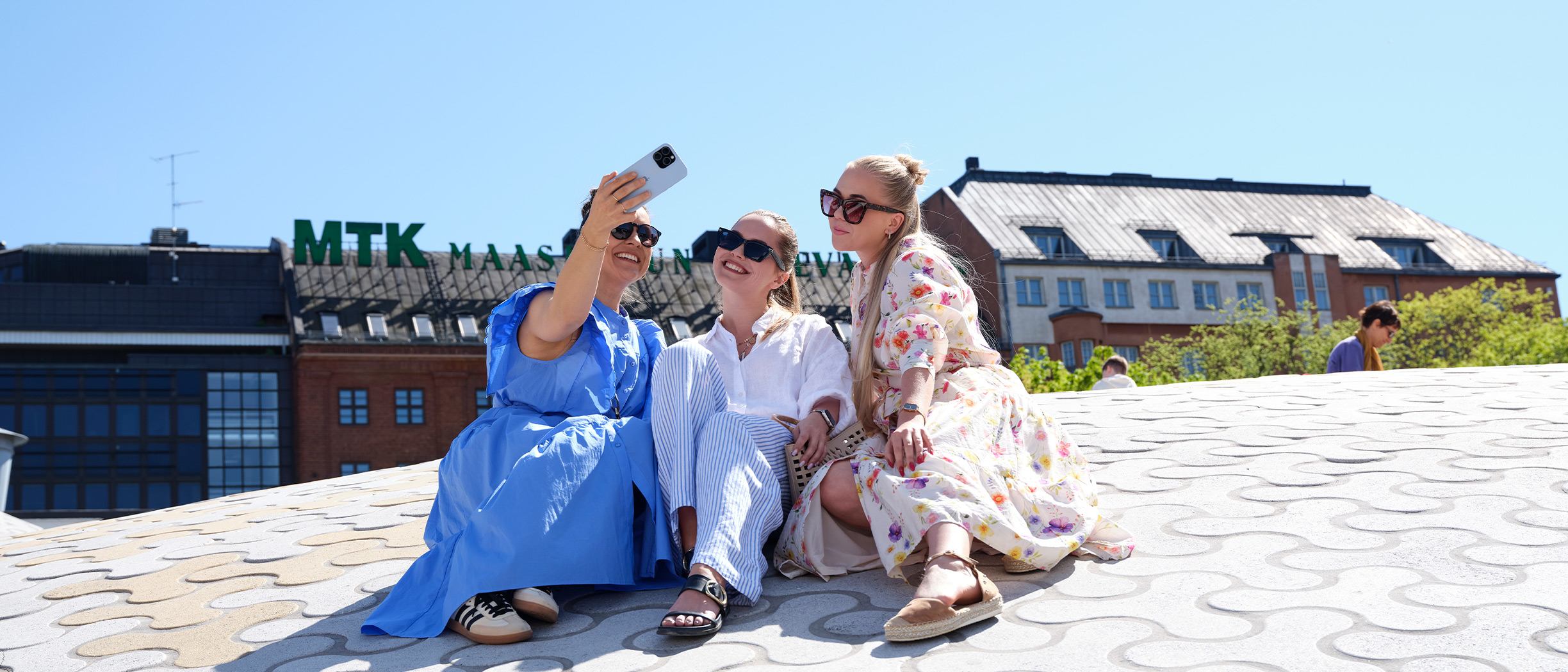 Tre kvinnor tar en selfie i solen vid Amos Rex i Helsingfors