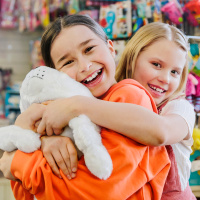 Två tjejer i en butk och håller om varandra och kramar ett gosedjur