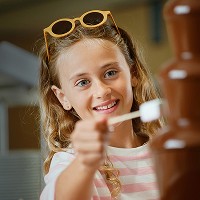 Nuori tyttö laittaa vaahtokarkin suklaaputoukseen Buffet-ravintolassa