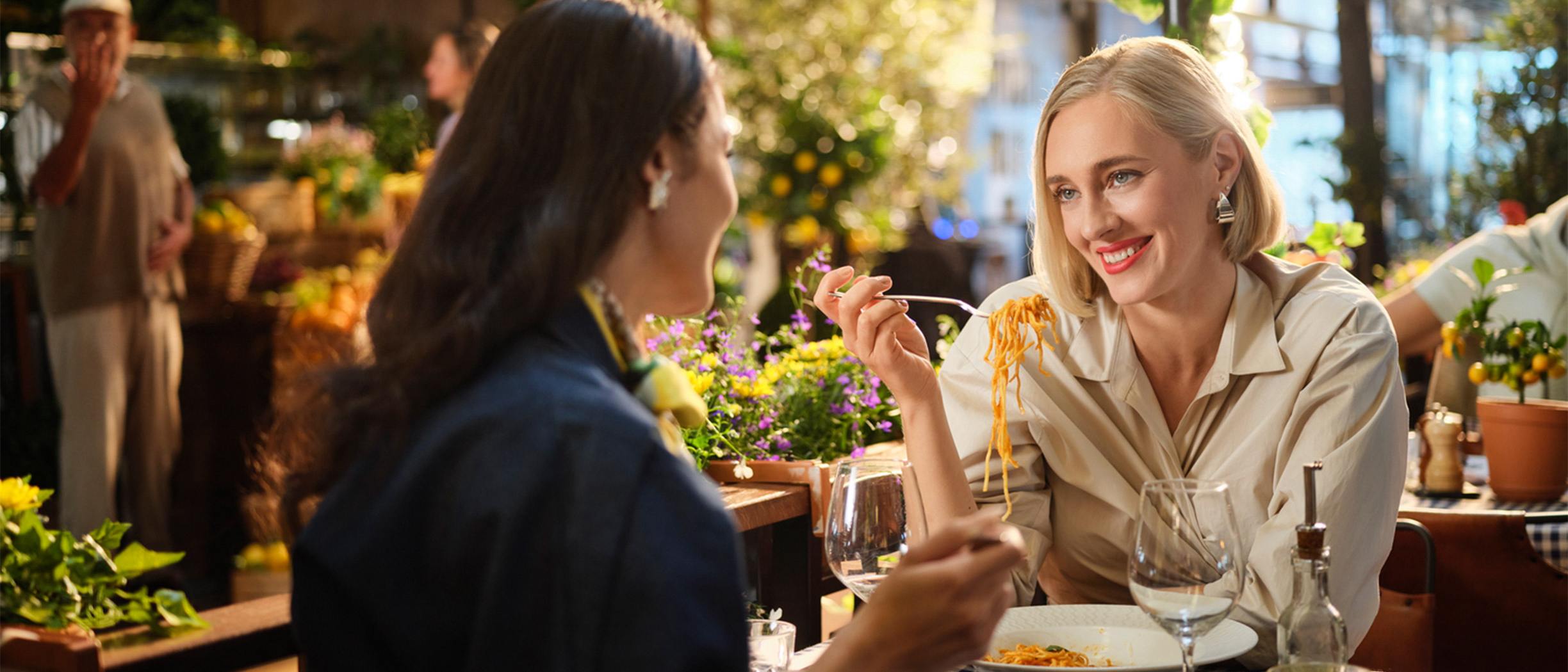 Two women onboard a cruise ship, talking and eating pasta